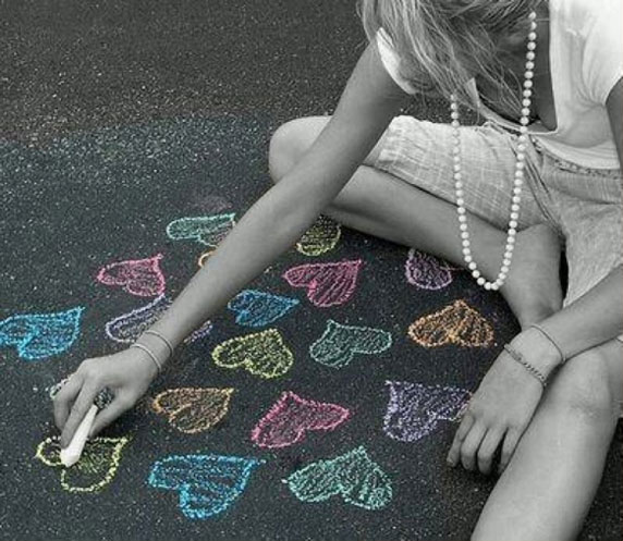 Uma menina desenhando com giz corações no chão.